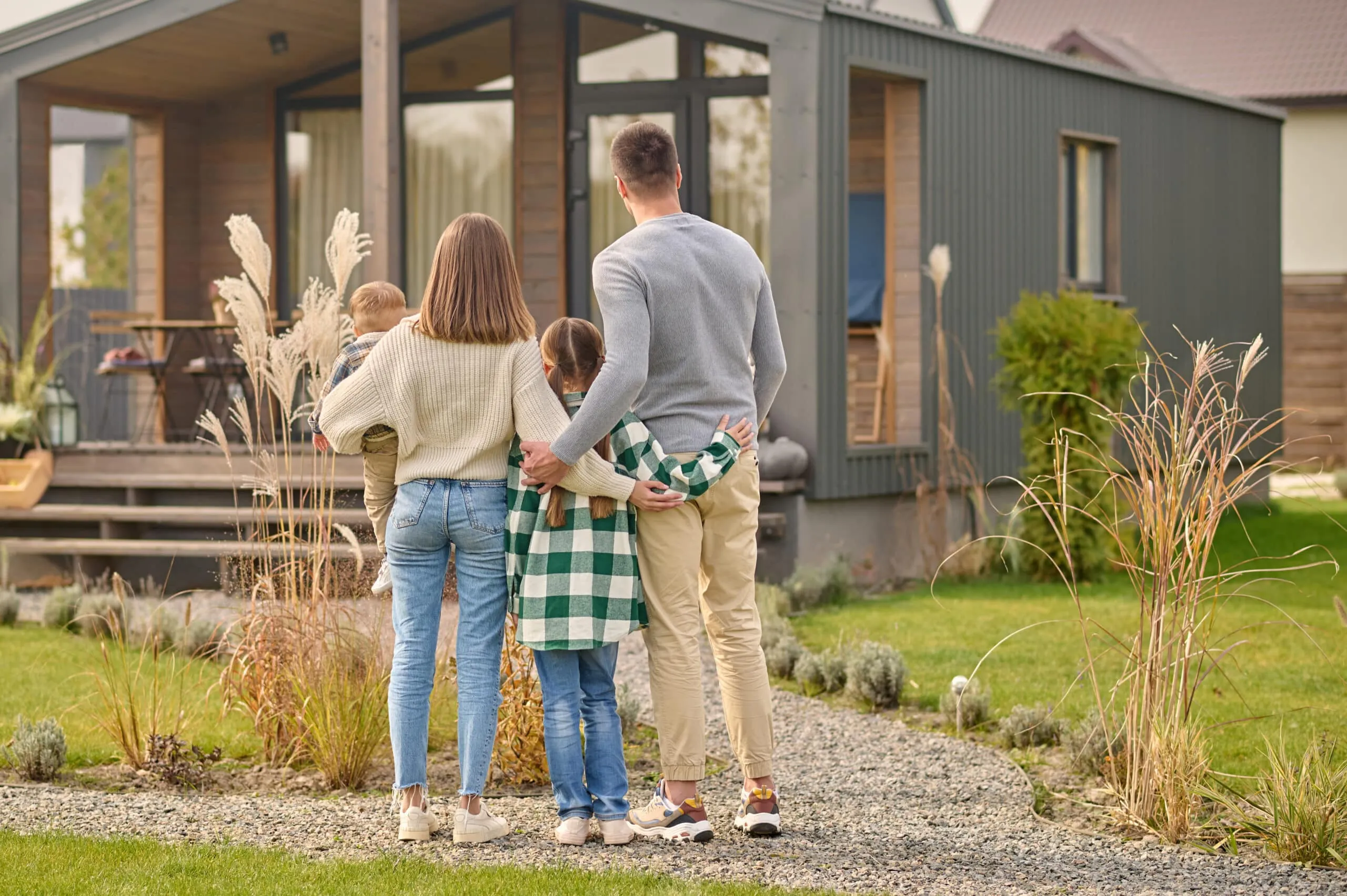 A family of four viewed from behind, arms around each other, facing their house.