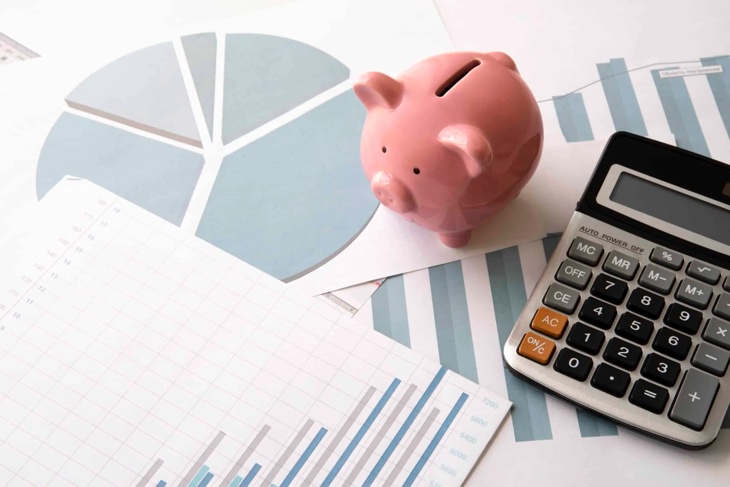 A pink piggy bank and calculator resting on printed pie charts and bar graphs.
