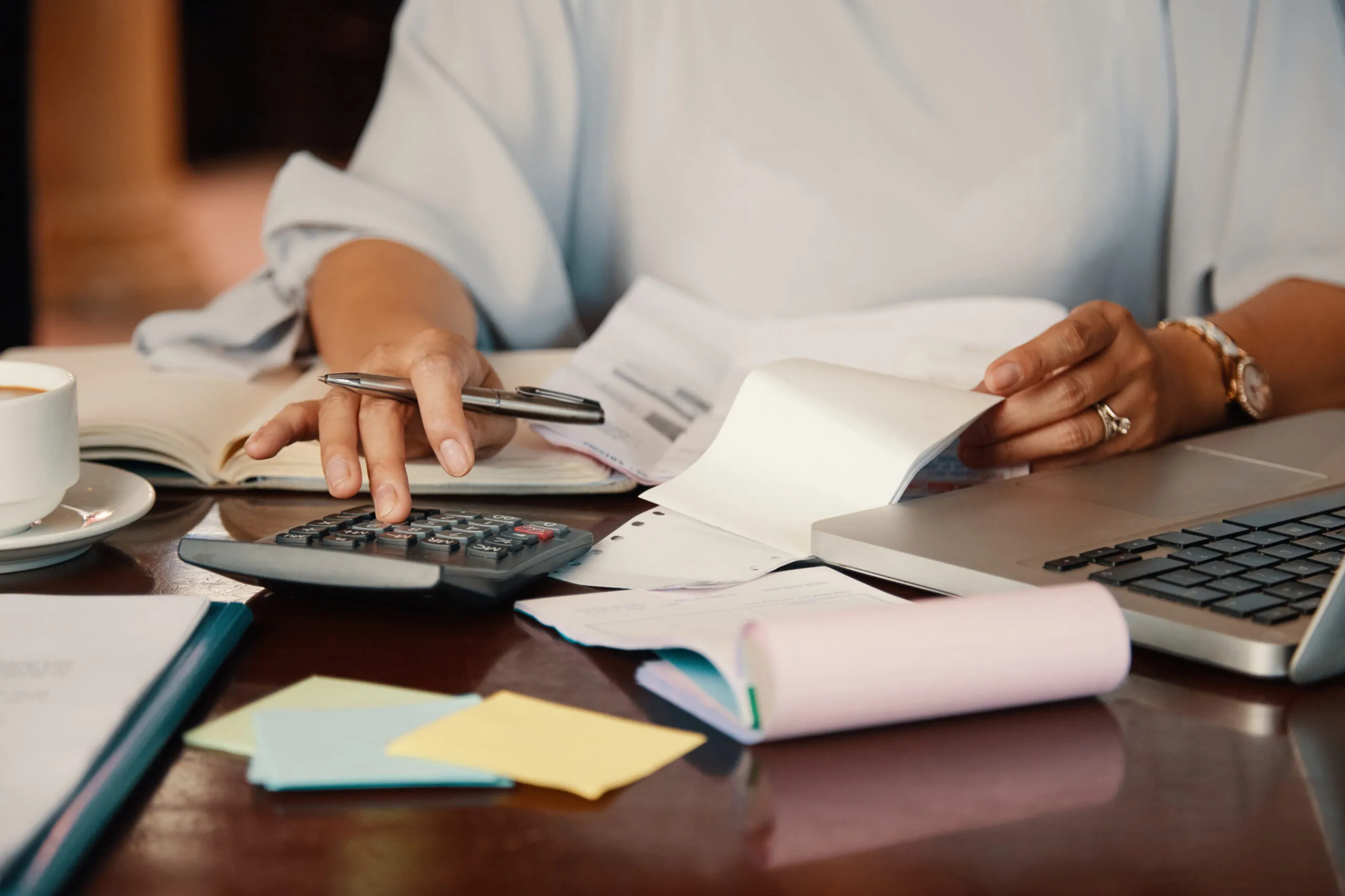 Close-up of hands using a calculator among bills, notebooks and a laptop