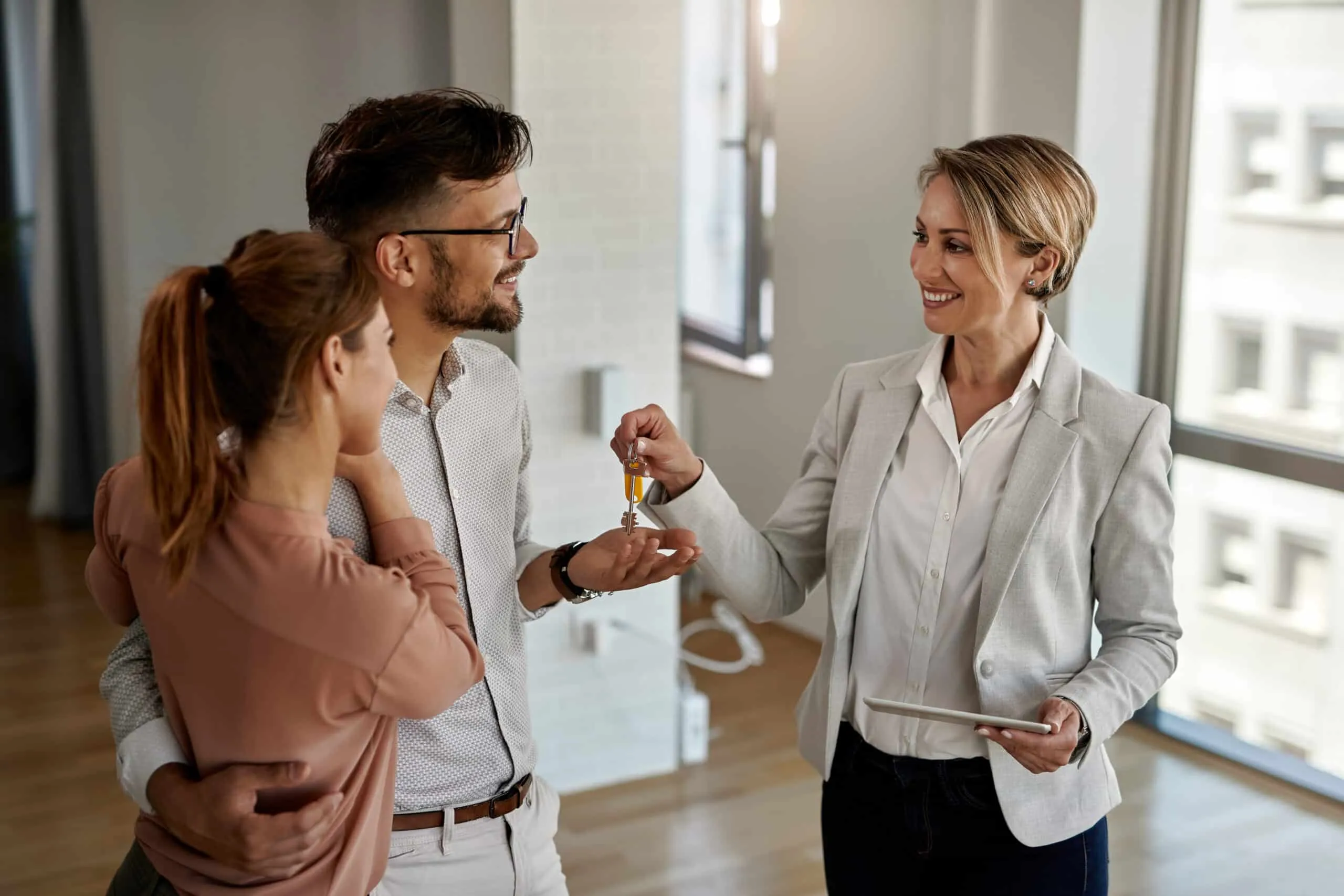 A real estate agent hands house keys to a smiling couple in an empty apartment