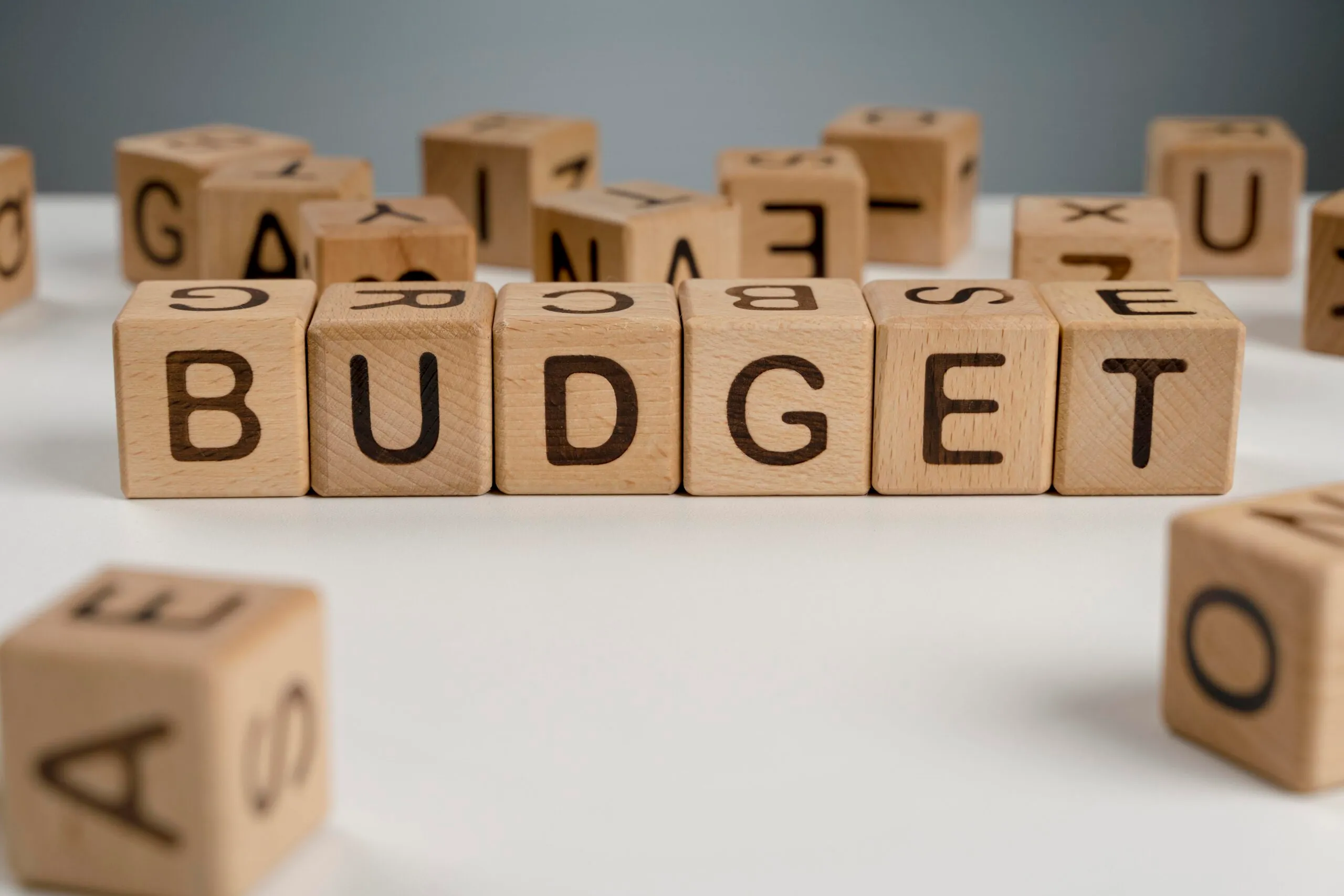 Wooden alphabet blocks spelling the word budget surrounded by scattered loose letter blocks