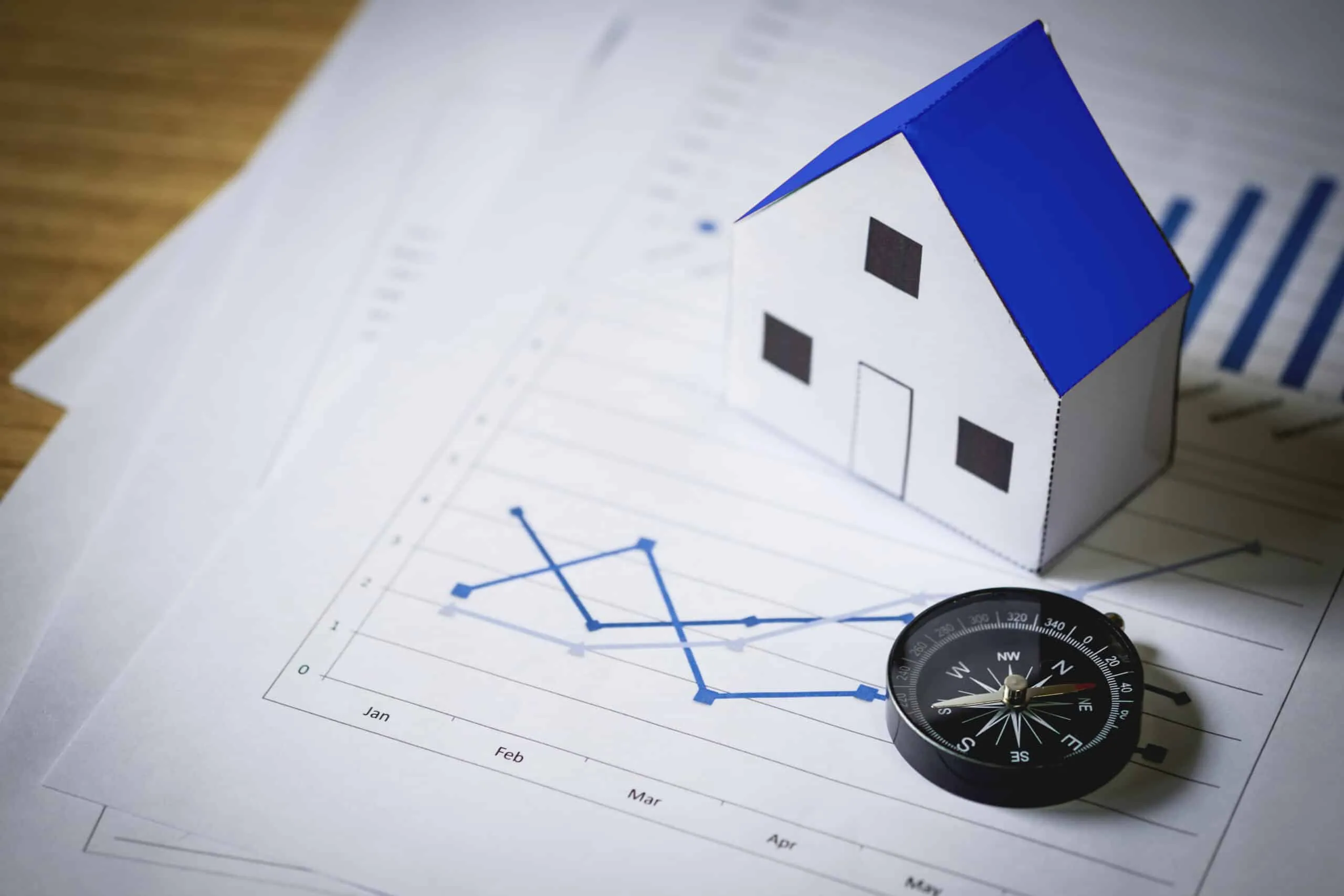 A small paper house model and compass resting on a printed line graph