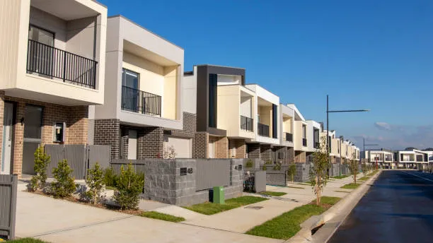 A row of modern townhouses with balconies along a suburban street under a blue sky