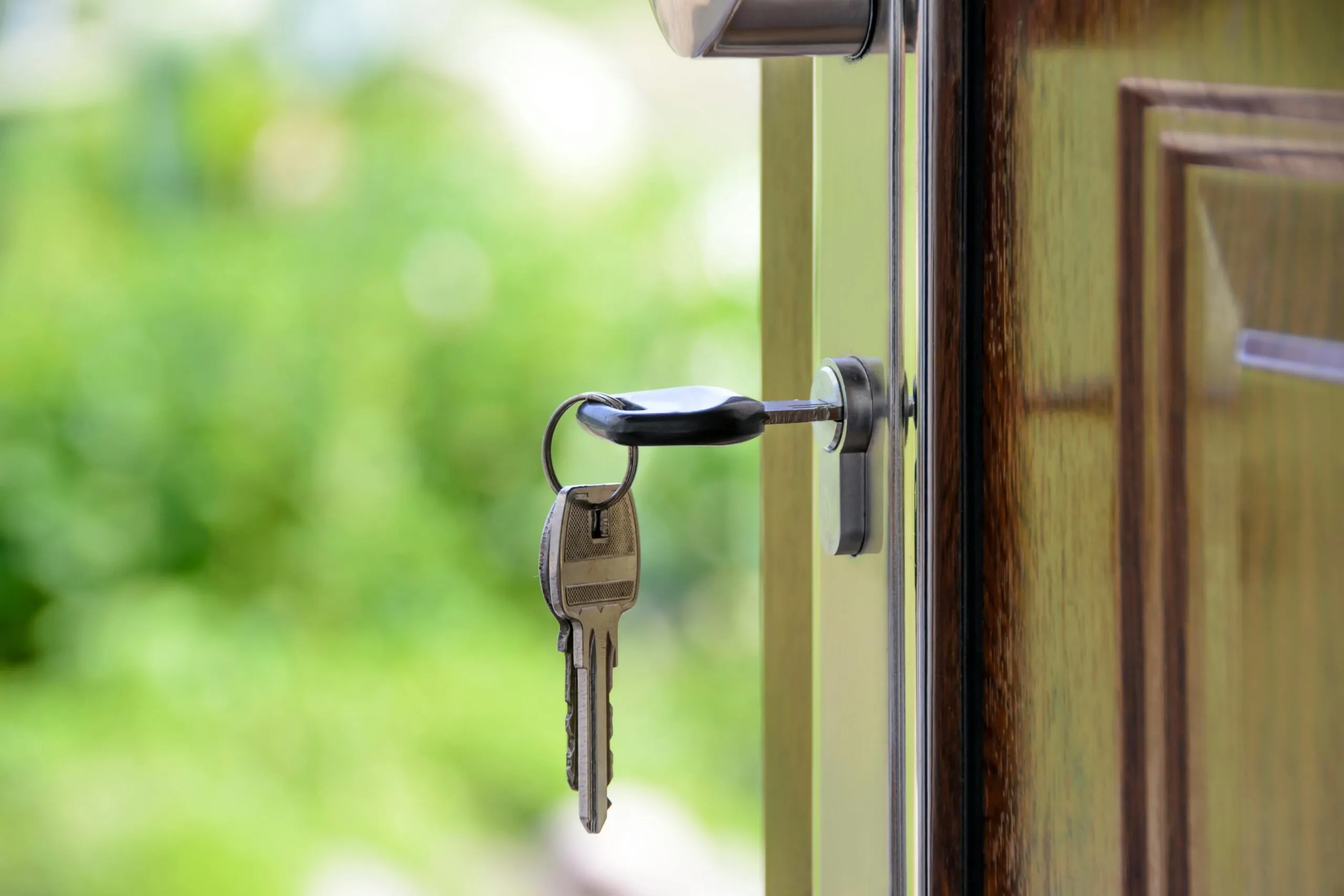 House keys left hanging in a glass front door lock, green garden blurred behind