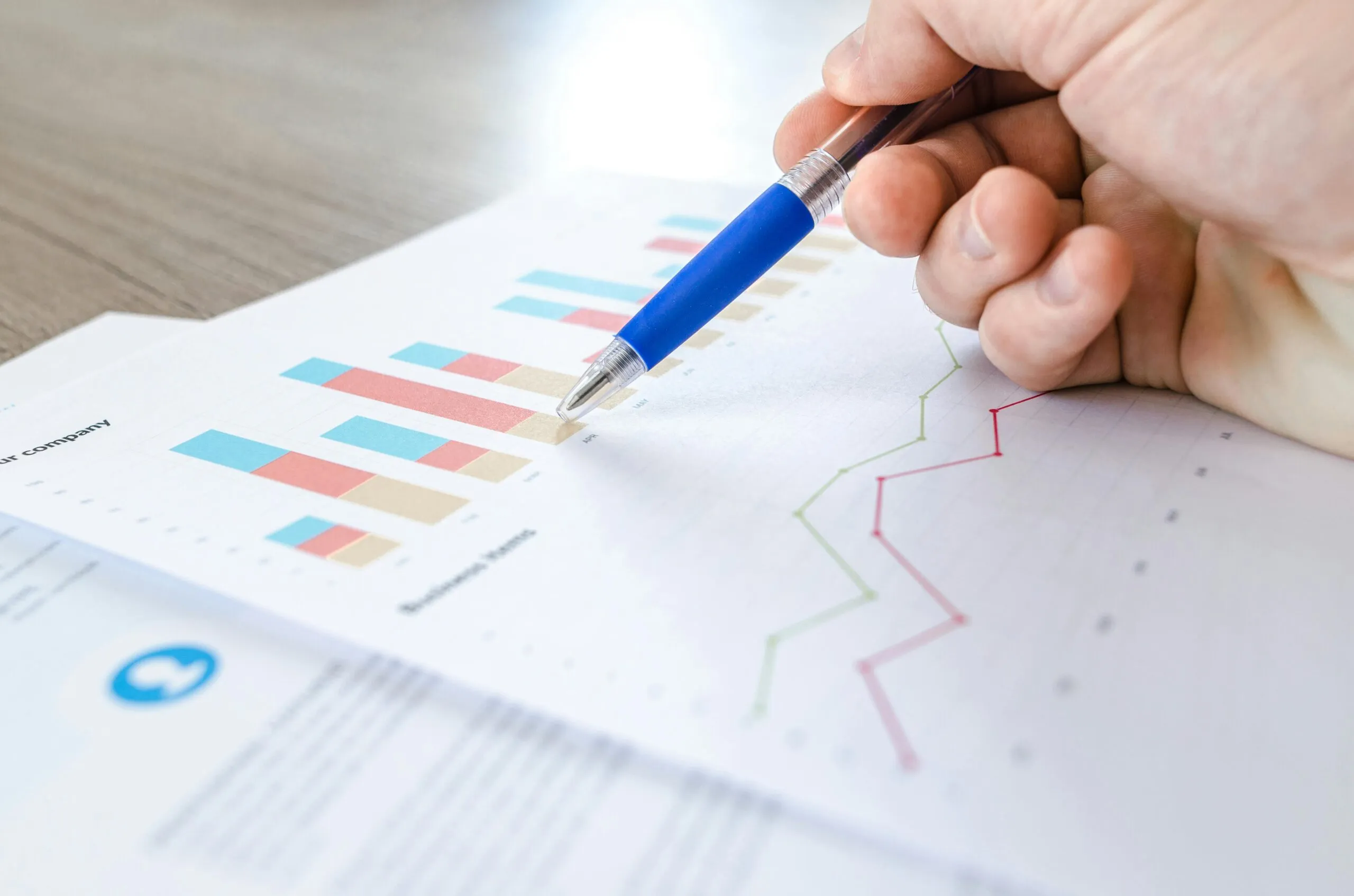 A hand holding a blue pen points to a printed bar and line chart report