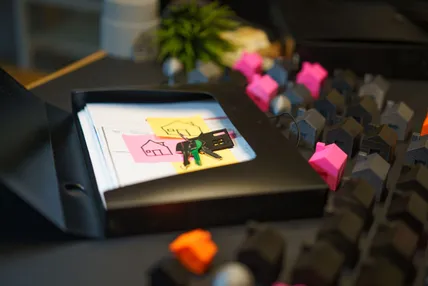 Keys and hand-drawn house sketches on a stack of paperwork, with miniature house models arranged on a desk in the background.