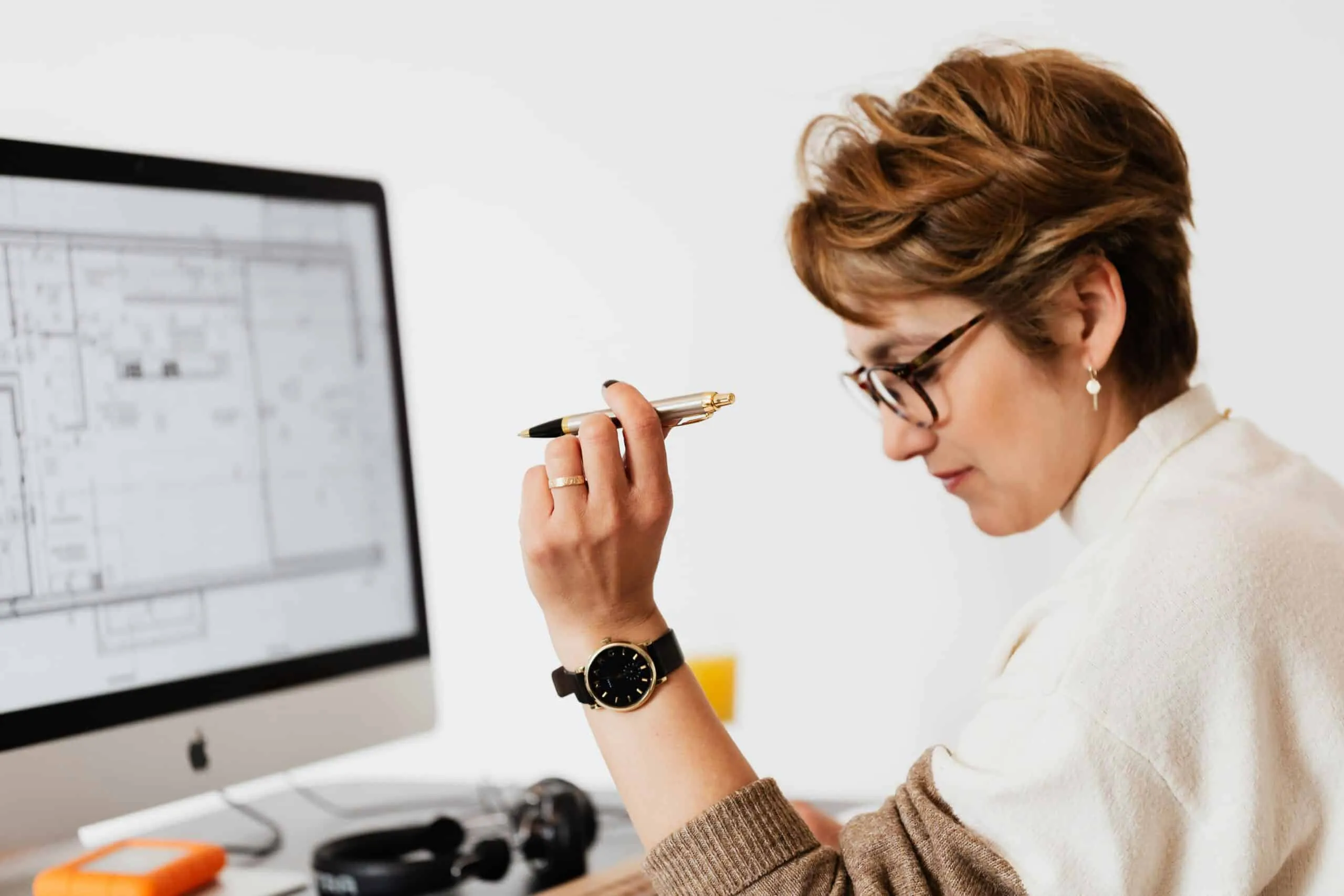 A woman wearing glasses holds a pen while studying a floor plan on screen