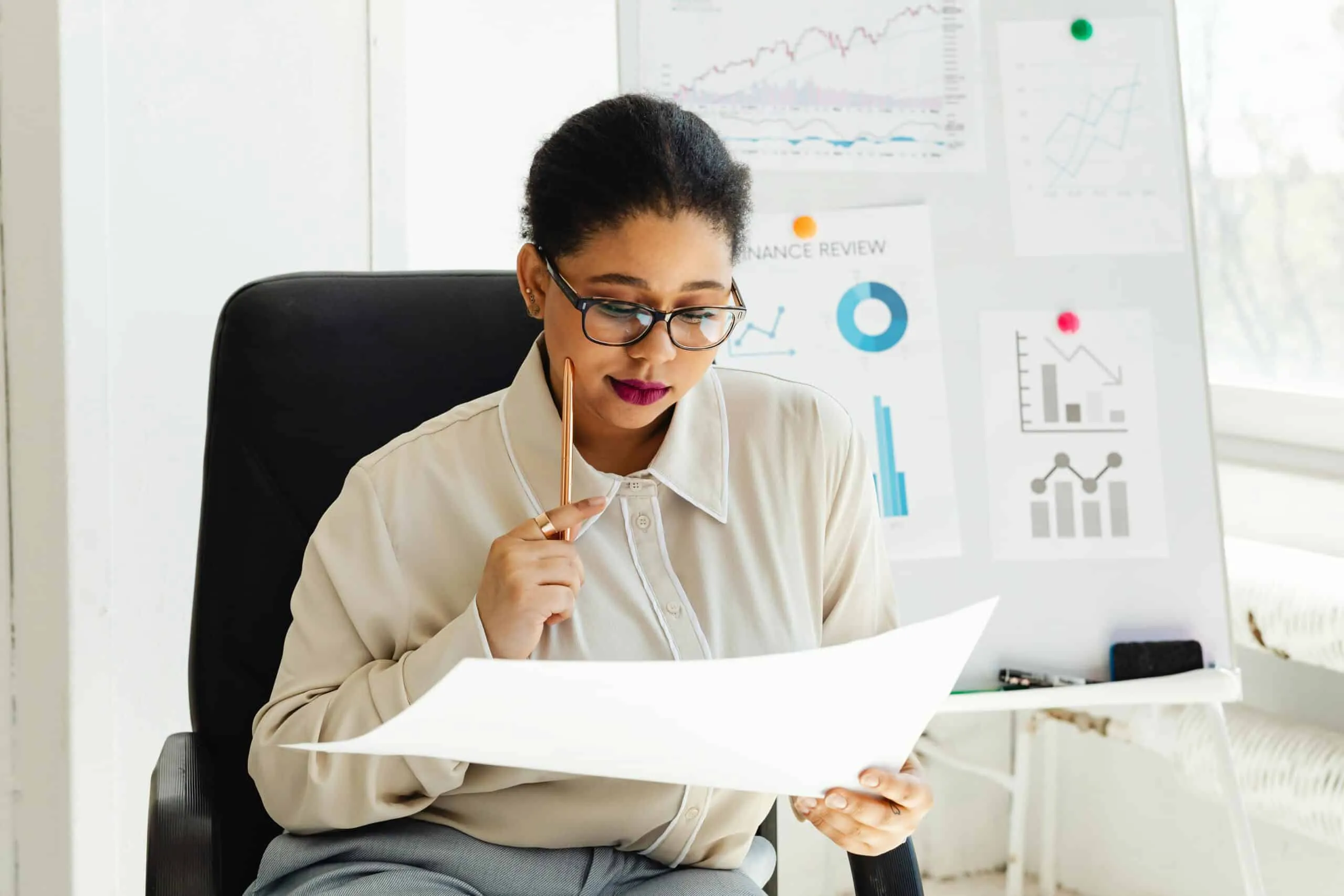 A woman sits in an office chair reviewing papers with charts pinned on the wall