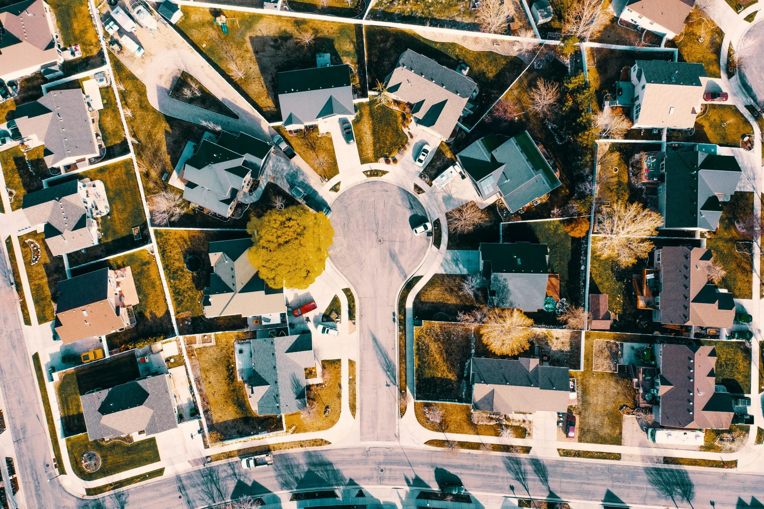 An aerial drone view of a suburban cul-de-sac with houses, driveways and a tree
