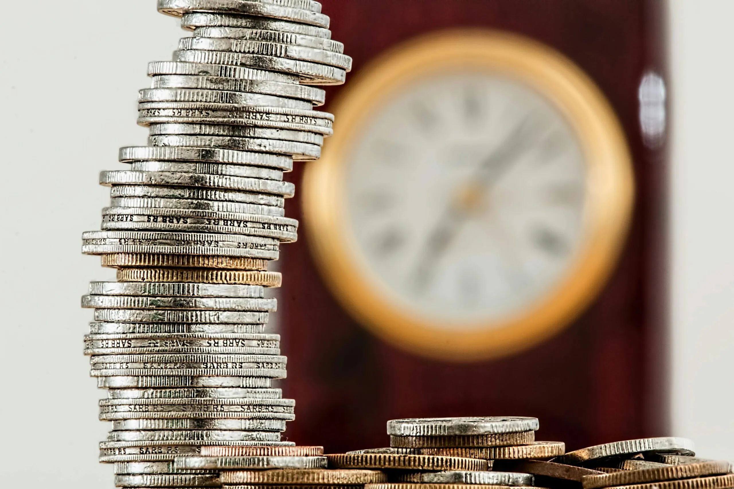 Stack of coins in the foreground with a blurred clock face in the background