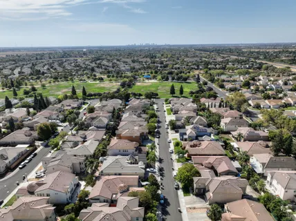 Aerial view of a suburban housing estate with rows of tiled roofs, streets and a central park.