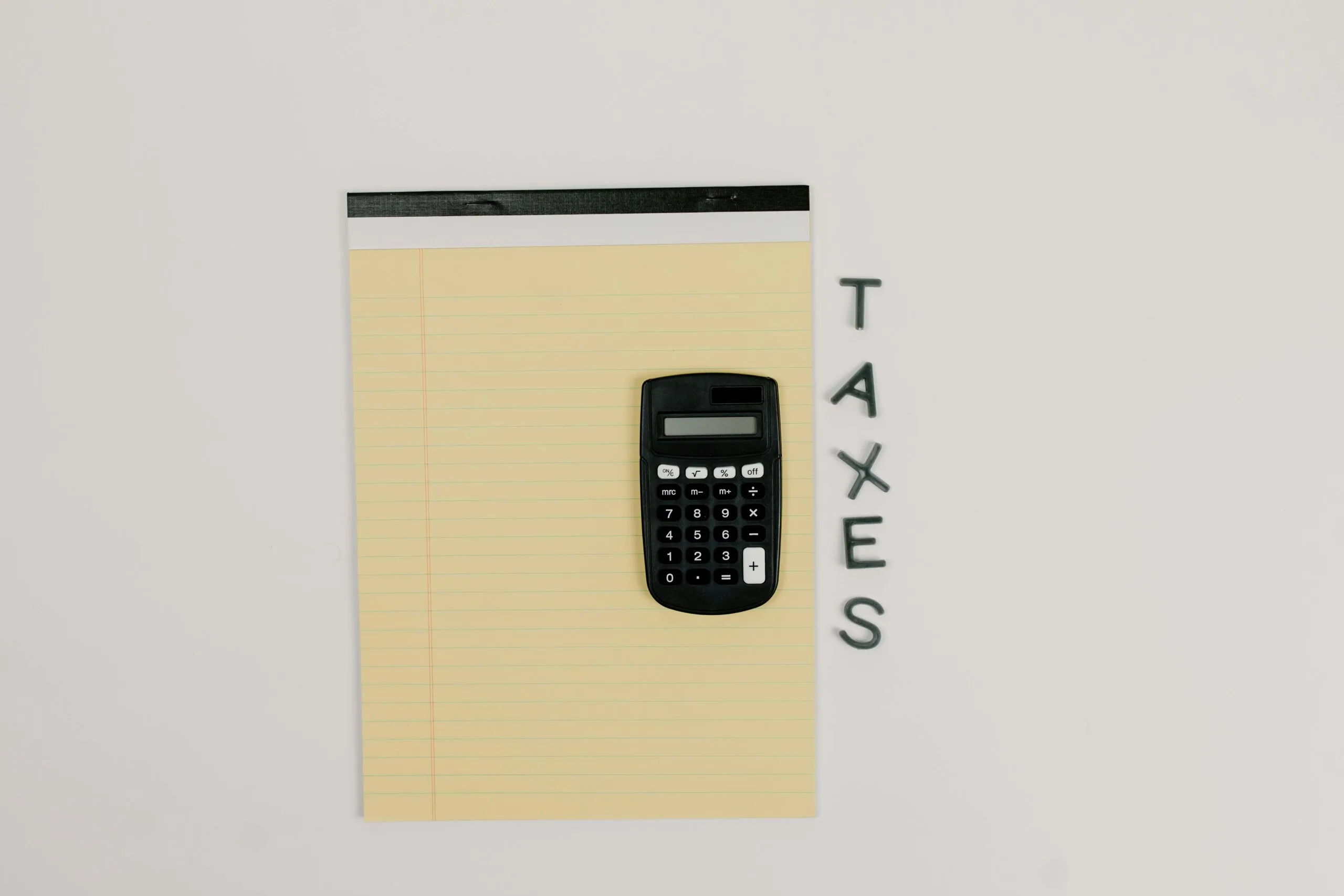 A calculator on a lined notepad beside wooden letters spelling TAXES on a table