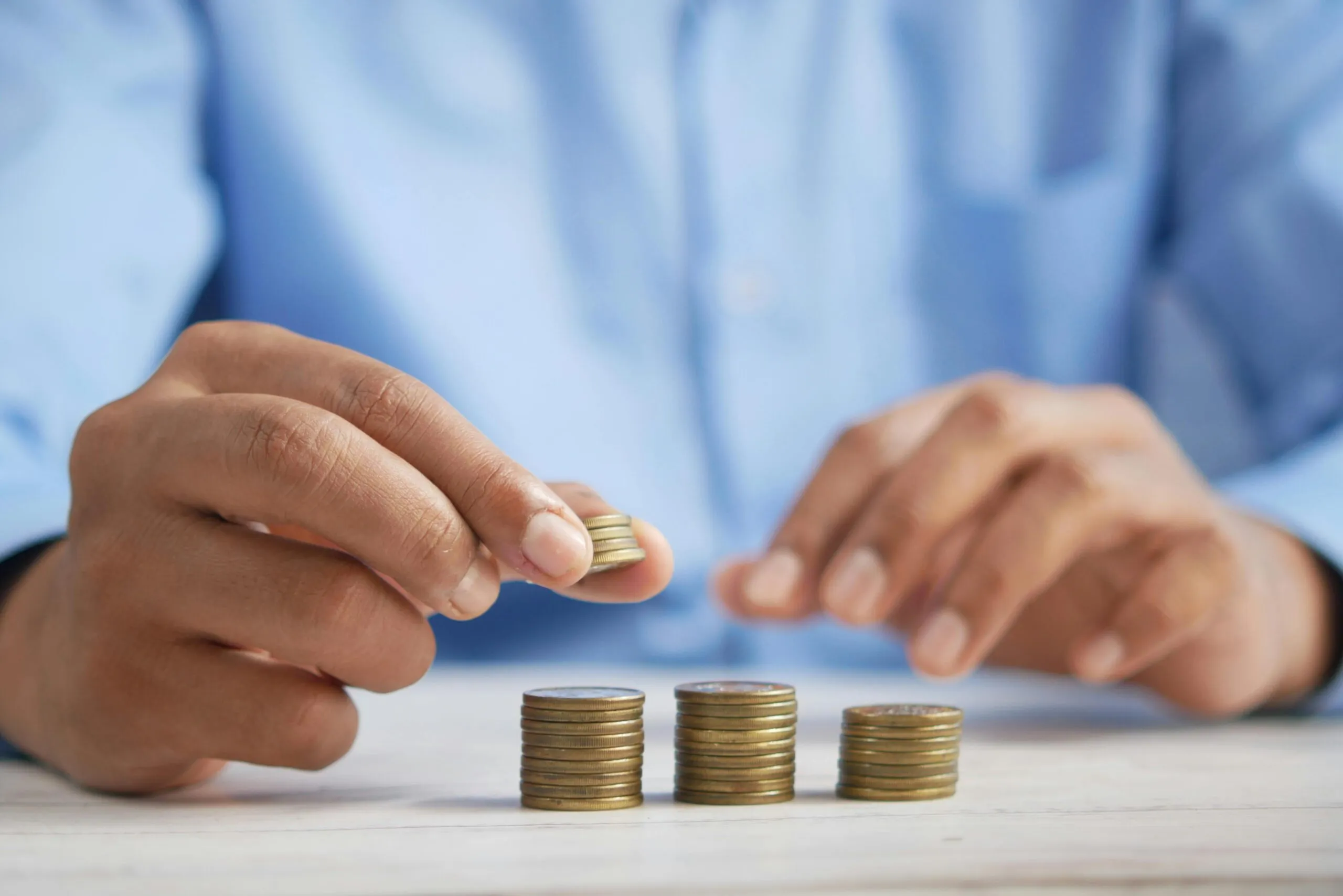 Close-up of hands stacking coins into three piles on a table
